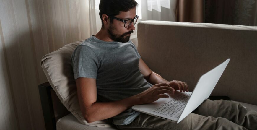 Remote Job. Man Working On Laptop Sitting On Sofa At Home.