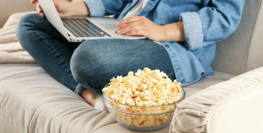 Woman watching film on sofa and eat popcorn. Food for watching films