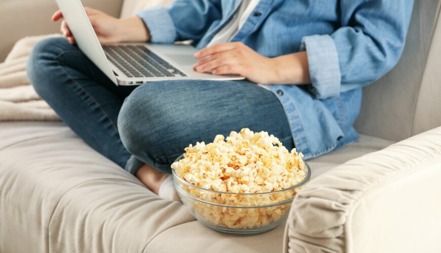 Woman watching film on sofa and eat popcorn. Food for watching films